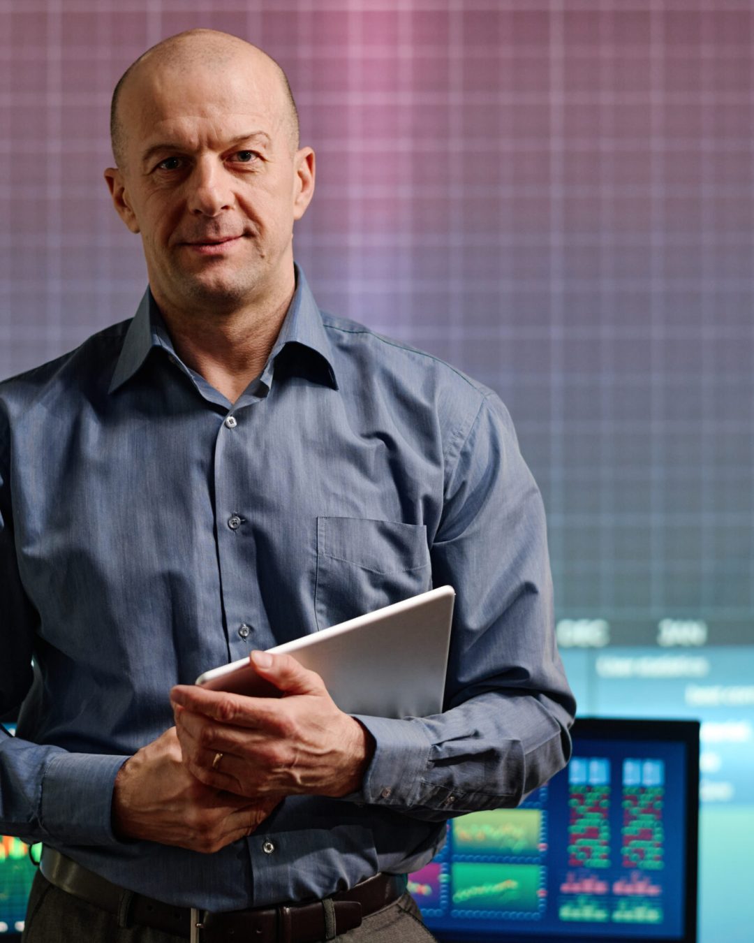 Portrait of mature Caucasian professional investment specialist standing in office holding digital tablet looking at camera